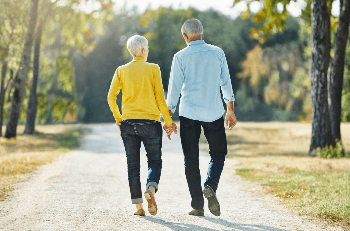 An elderly couple walking away holding hands.