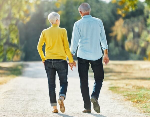 An elderly couple walking away holding hands.