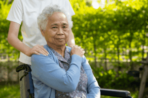 A senior woman in a wheelchair accompanied by a helper.
