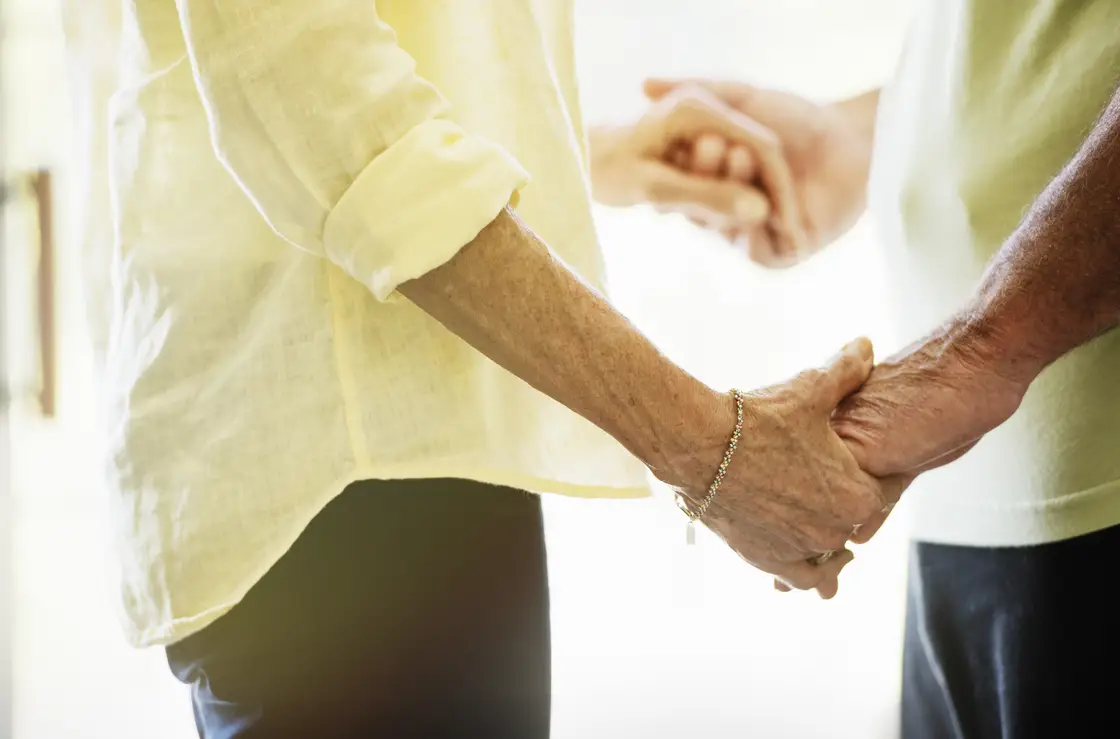elderly couple sharing hands indoors