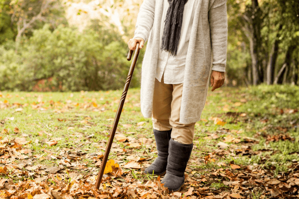 An elderly person with a cane walking amongst leaves.